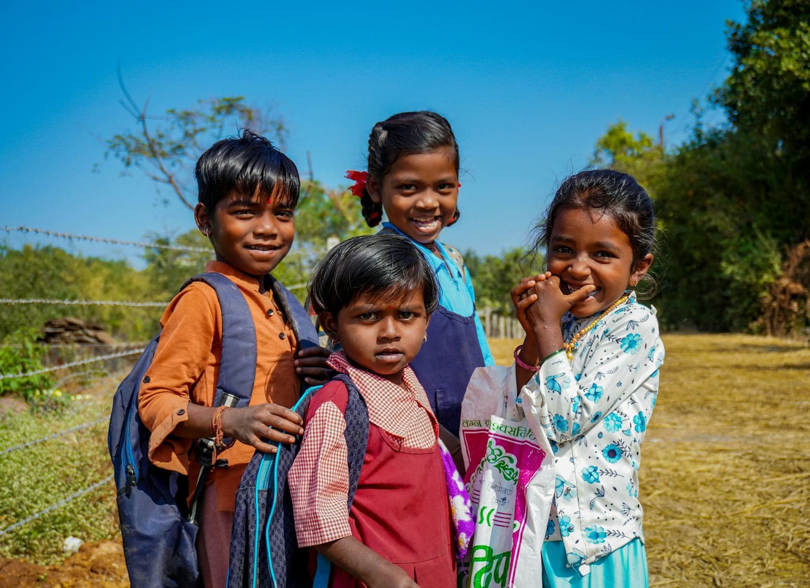 Four smiling students with school bags outdoors